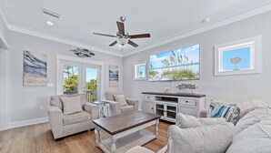 A spacious living room with a ceiling fan, a large window with a view of the outdoors, a dining table, and a sofa.