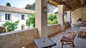 Une terrasse extérieure avec une table et des chaises en osier, donnant sur un bâtiment blanc avec des volets.