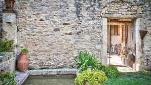 Un bâtiment en pierre avec une petite cour, une porte en bois et un portail en métal.