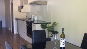 Une cuisine moderne avec des meubles blancs, un plan de travail noir et un coin repas comprenant une table et des chaises en verre.
