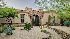 A stucco house with a stone facade, a black gate, and a desert garden with cacti and agave plants. - Desert Oasis with Pool & Black Mountain Views! (Scottsdale)