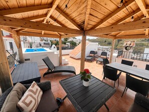A covered outdoor seating area with a pool, chairs, and a table.