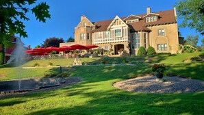 A large, stately building with a prominent entrance, a well-maintained lawn, and red umbrellas in the foreground. - Experience Divine Serenity, Nature & Luxury - Unite. Rest. Reflect. Restore (Pembroke)