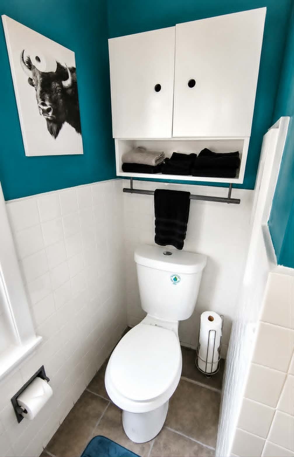 A small bathroom with a toilet, a shelf with folded towels, and a toilet paper holder.