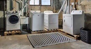 A laundry room with a washing machine, dryer, and stacked laundry baskets on wooden pallets. - The Buffalo Loft- 3BR Upstairs Apartment • Pet-Friendly • Outdoor Patio &... (Buffalo)