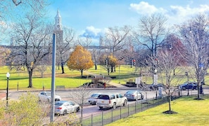 Un parc avec un beffroi, une allée pavée et des voitures garées.