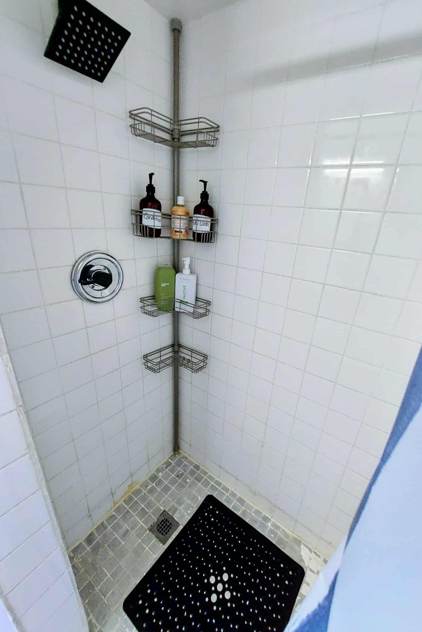 Een kleine, betegelde douchecel met een metalen rek voor toiletartikelen.