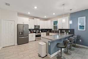 A modern kitchen with white cabinets, stainless steel appliances, and a central island with bar stools.