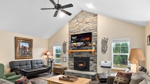 A living room with a stone fireplace, leather sofa, and a flat-screen TV mounted above the fireplace. - Raintree at Roslyn Ridge - Cozy Retreat (Ronald)