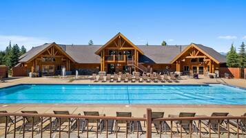 A lodge with a large pool, outdoor seating, and a mountain backdrop.