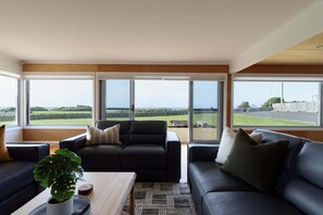 Een moderne woonkamer met een groot raam, een zwarte leren bank, een houten salontafel en een potplant.