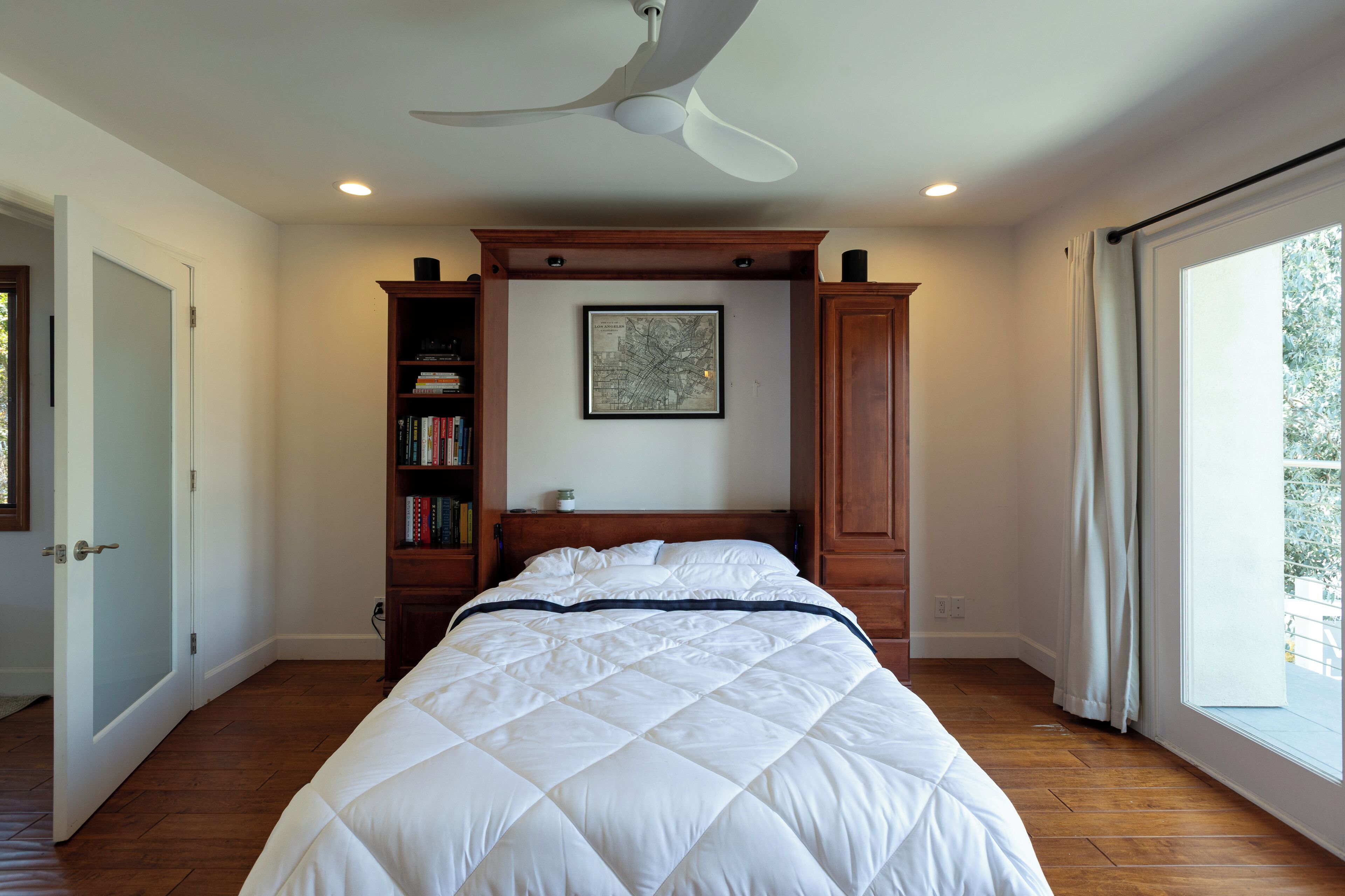 Une chambre à coucher avec un lit, un ventilateur de plafond, une bibliothèque et une fenêtre.