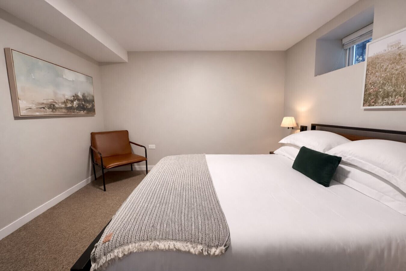 A hotel room with a large bed, a chair, a lamp, and two paintings on the walls.