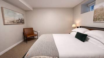 A hotel room with a large bed, a chair, a lamp, and two paintings on the walls.