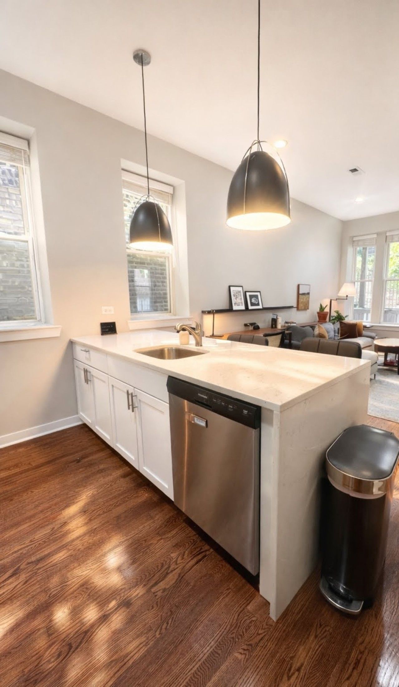 A modern kitchen with a central island, stainless steel dishwasher, pendant lighting, and hardwood flooring.