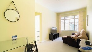 Una sala de estar con una mesa de vidrio, un sofá, un televisor y un ventanal con cortinas.
