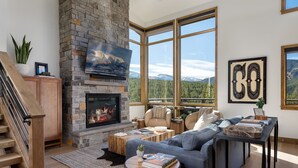 Una sala de estar moderna con chimenea de piedra, ventanas amplias y un rincón de estar acogedor.