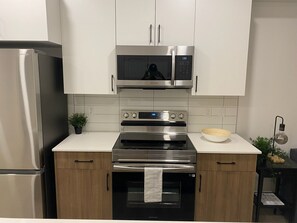 A modern kitchen with stainless steel appliances, including a refrigerator, microwave, and oven, with wooden cabinets and a white countertop.