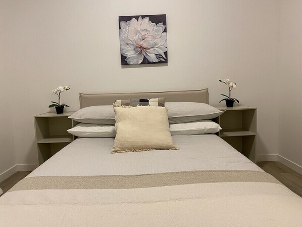 A neatly arranged bedroom with a bed, pillows, a bedside table, and a wall-mounted flower painting.