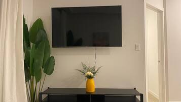 A living room with a flat-screen TV mounted on the wall, a black TV stand with a yellow vase, and a large green plant.