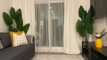 Un salon avec un canapé gris, un vase jaune et de grandes plantes vertes.