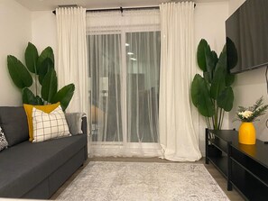 Uma sala de estar com um sofá cinza, um vaso amarelo e plantas verdes grandes.
