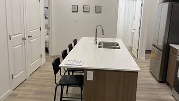 Une cuisine moderne dotée d’un îlot central, de meubles blancs et d’un réfrigérateur encastré.