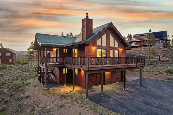 A large, rustic cabin with a prominent deck and multiple windows, surrounded by a natural landscape.