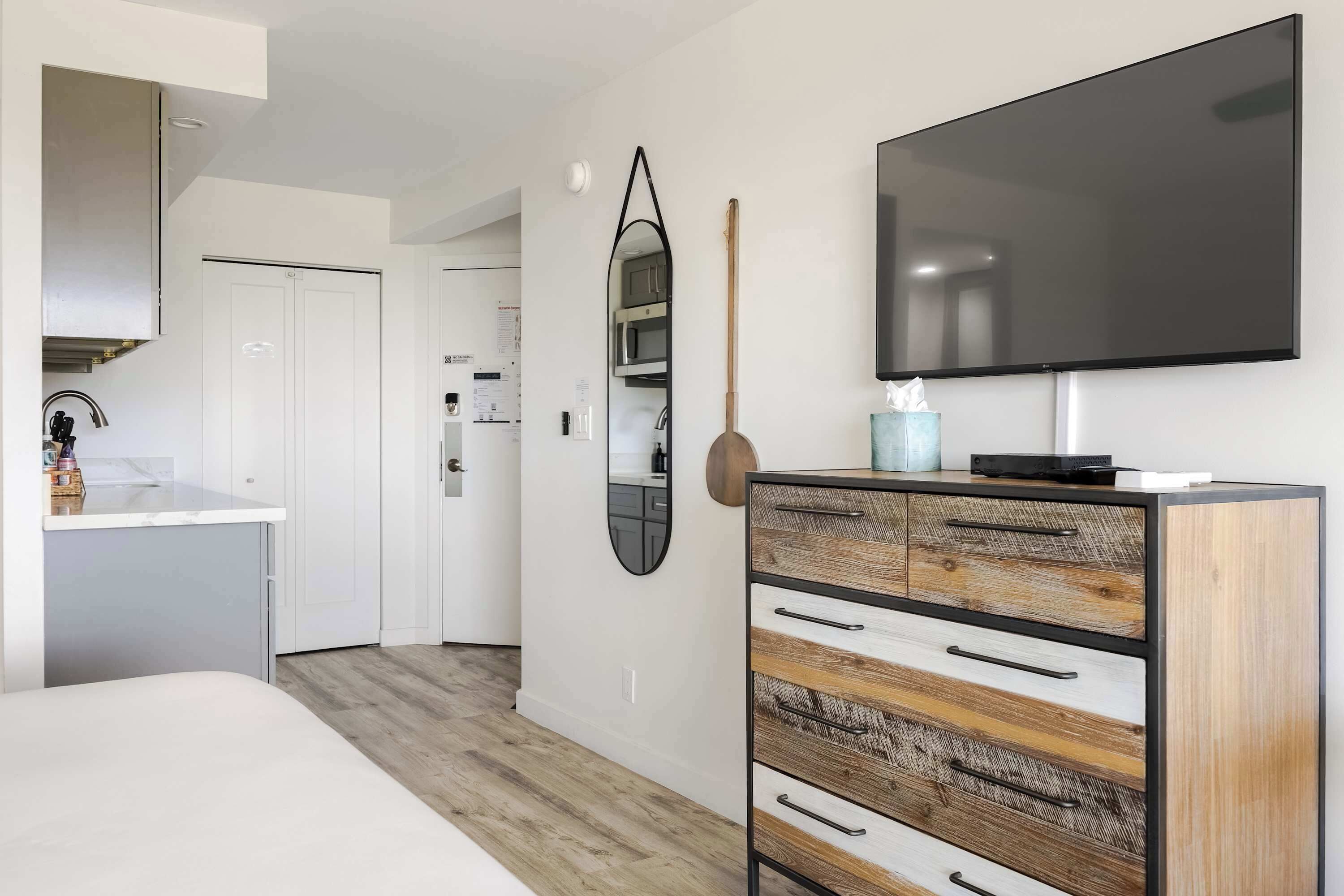 A modern bedroom with a large bed, a dresser with multiple drawers, a flat-screen TV, and a mirror on the wall.
