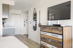 A modern bedroom with a large bed, a dresser with multiple drawers, a flat-screen TV, and a mirror on the wall.