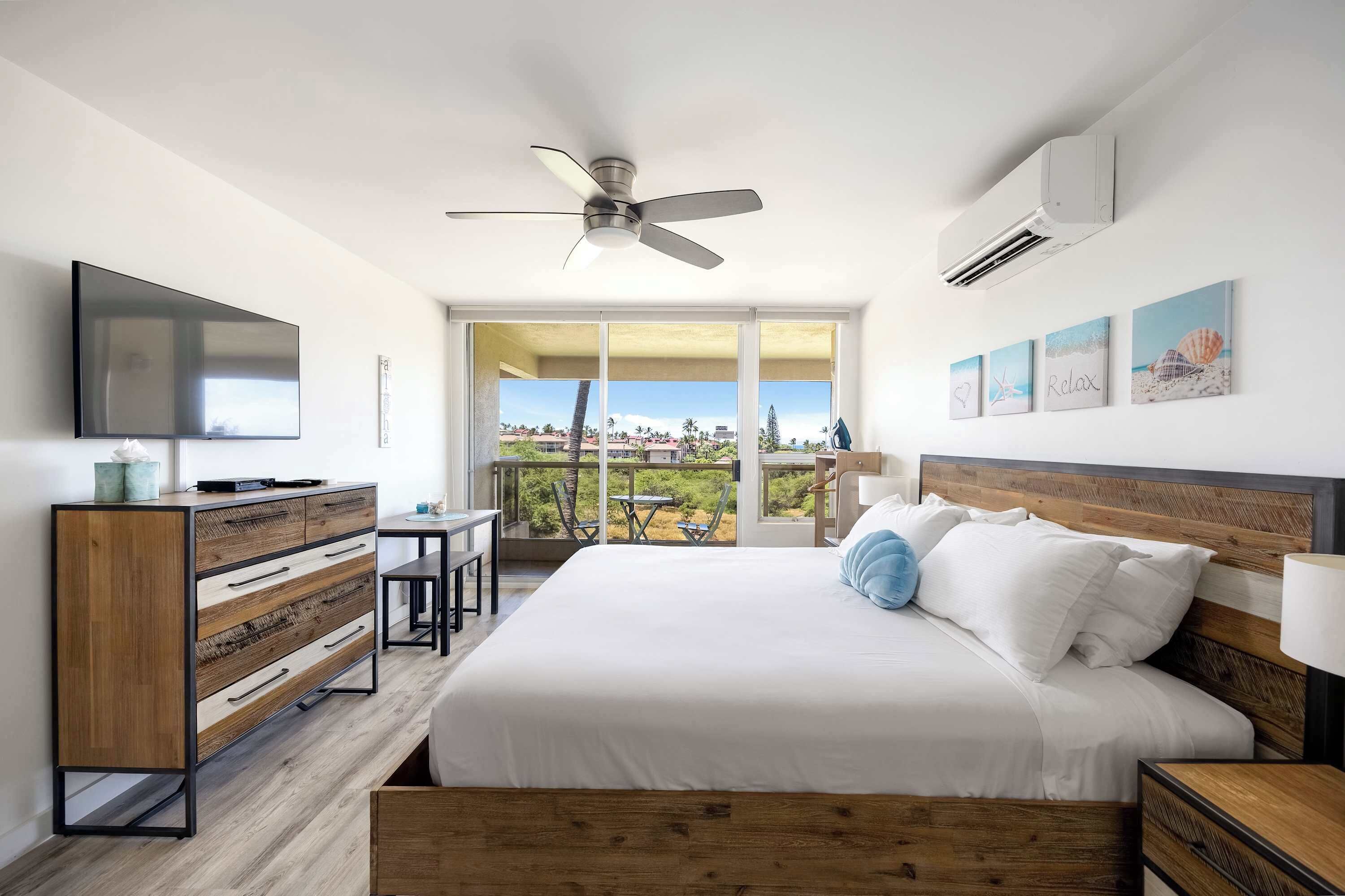 A modern bedroom with a bed, a desk, a ceiling fan, and a large window with a view.