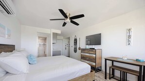 Un dormitorio moderno con cama, ventilador de techo, televisor y una mesita.