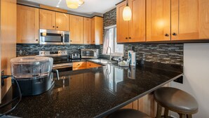 A modern kitchen with wooden cabinets, stainless steel appliances, a granite countertop, and pendant lighting. - Sunset Soul at Pelican Cove Unit 8 by SeaBreeze Vacation (Bradenton Beach)