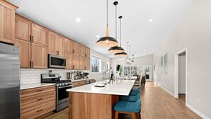 Een moderne keuken met houten kastjes, roestvrijstalen apparatuur, een groot kookeiland met barstoelen en hanglampen.