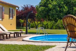 A swimming pool with lounge chairs and a chair, surrounded by a well-maintained lawn and trees.