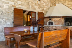 A stone-walled room with a wooden bench, a table, and a brick fireplace.