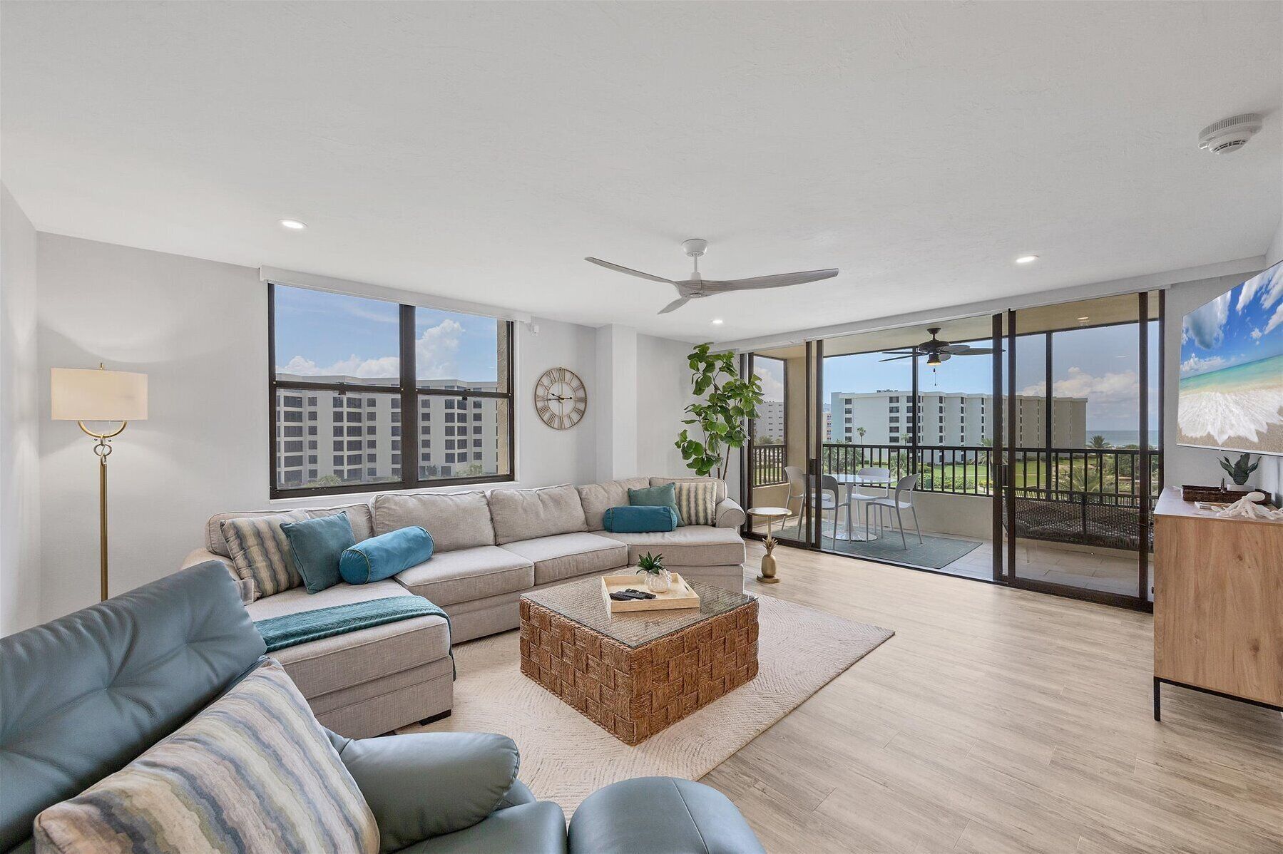 A spacious living room with a large sofa, a coffee table, and a balcony with a view of the cityscape.