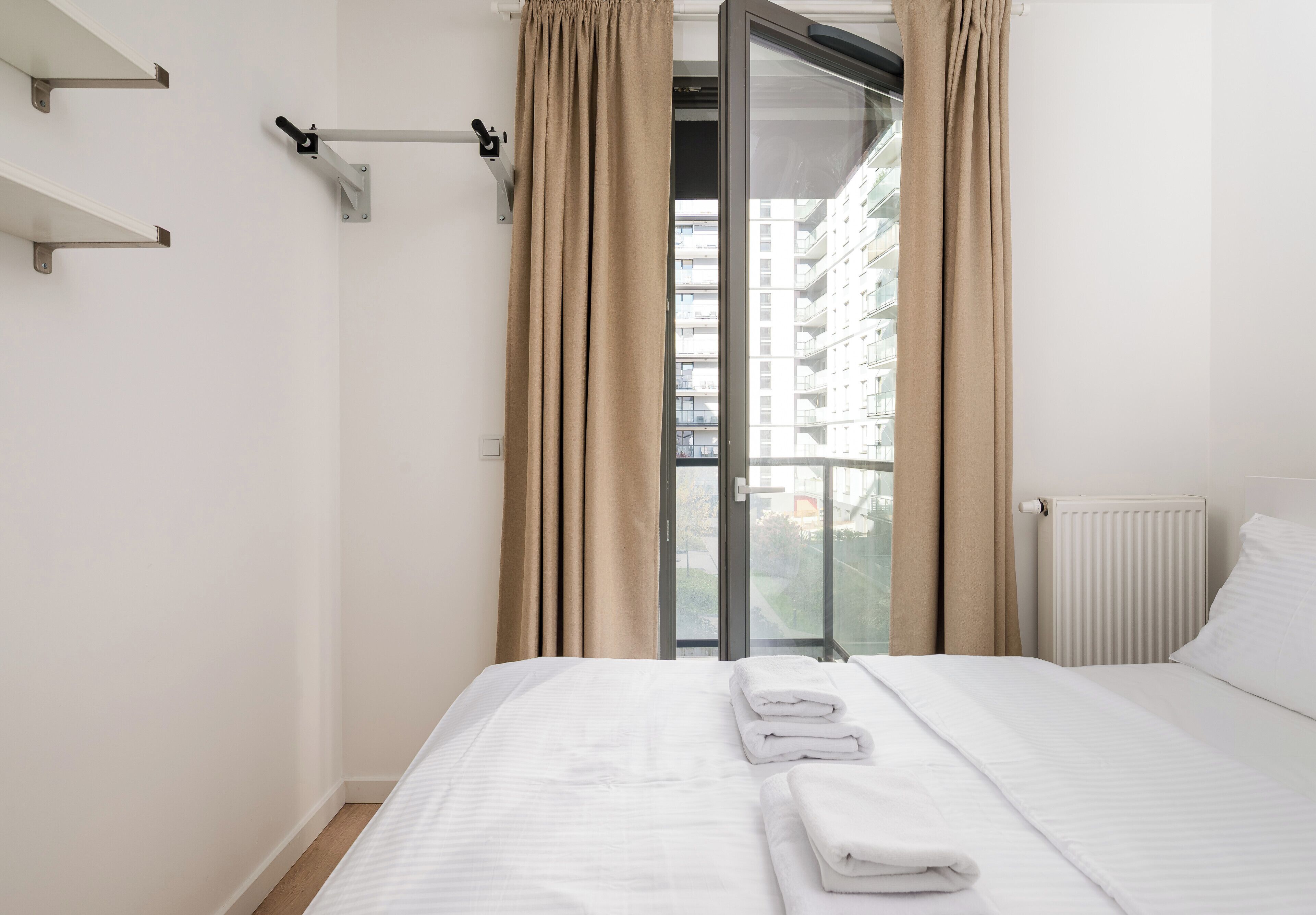 Habitación de hotel con cama, ventana con cortinas, radiador y vista a un edificio.