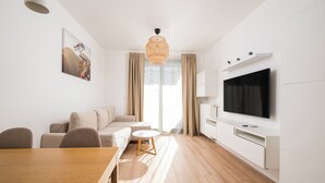 A modern living room with a wooden dining table, a sofa, a TV, and a large window with curtains. - Wola Signature Apartment (Warszawa)
