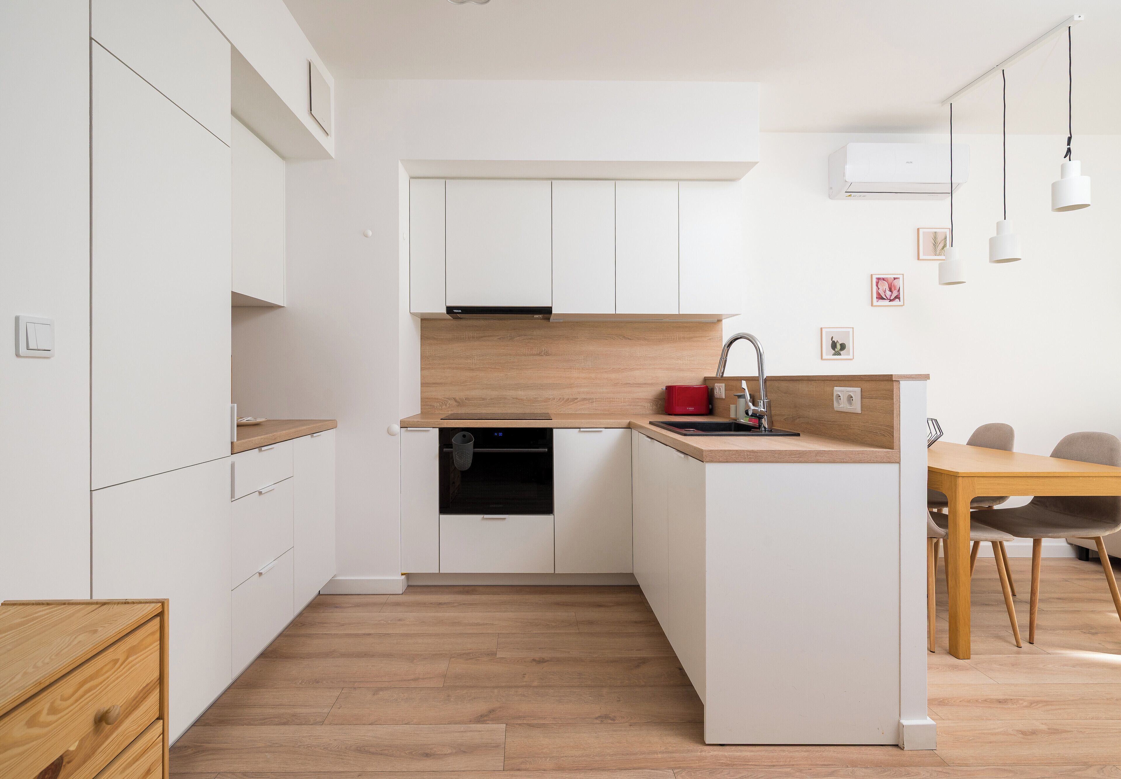 Eine moderne Küche mit weißen Schränken, einer Holz Arbeitsplatte und einem eingebauten Geschirrspüler. Ein Essbereich mit Holztisch und Stühlen ist ebenfalls vorhanden.