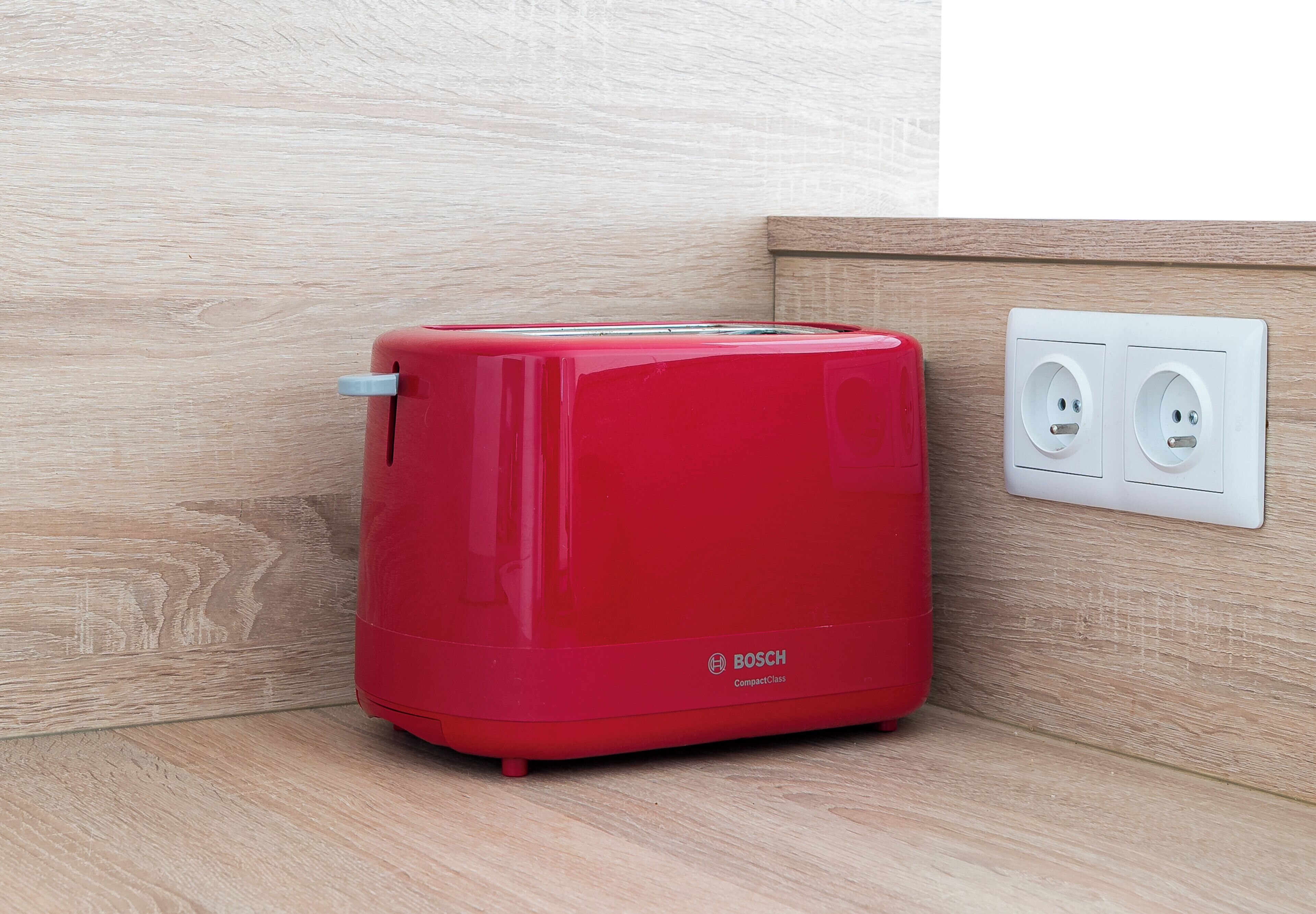 Un tostador compacto rojo Bosch sobre una encimera de madera junto a un enchufe de pared.