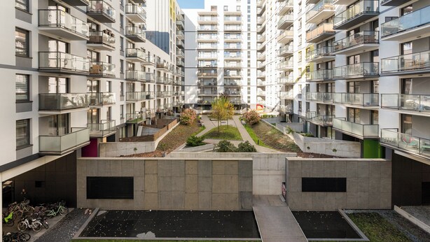 A modern apartment complex with multiple balconies, a central courtyard with trees, and a bike parking area. - Wola Signature Apartment (Warszawa)