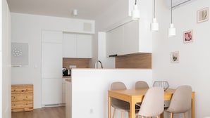 A modern kitchen with white cabinets, a wooden dining table, and four chairs. - Wola Signature Apartment (Warszawa)