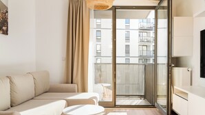 A modern living room with a sofa, a small round table, and a sliding glass door leading to a balcony. - Wola Signature Apartment (Warszawa)