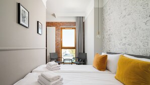 A hotel room with two beds, a brick wall, a window with curtains, and a view of the street.