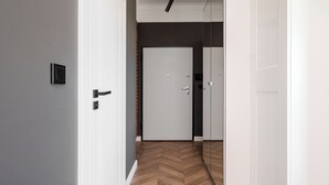 A hallway with a herringbone-patterned wooden floor, white walls, and a closed door at the end.