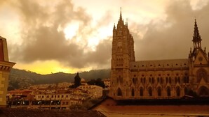 A cathedral with Gothic architecture, a cityscape with buildings, and a cloudy sky.
