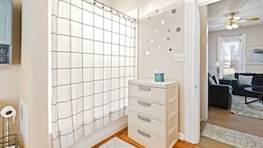Une salle de bain avec un rideau de douche à motifs géométriques, un meuble de rangement blanc doté de tiroirs et des toilettes bien visibles.