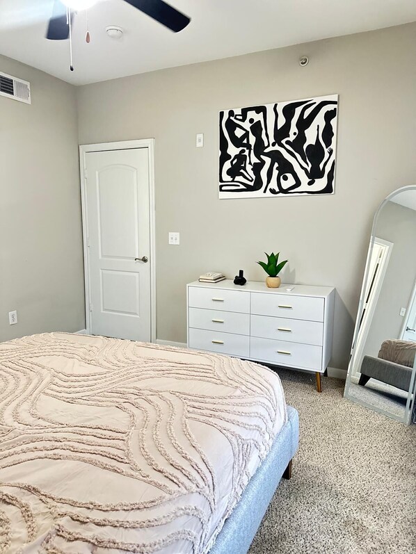 Un dormitorio con cama, cómoda, espejo y una obra de arte en la pared.