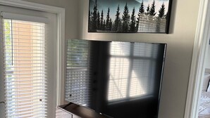 Un salon avec un téléviseur à écran plat fixé à un meuble en bois, une porte avec des stores et un sol recouvert d’une moquette.